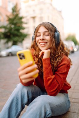 Genç, neşeli, güzel bir kadın dans ediyor ve kulaklıkla en sevdiği müziği dinliyor. Seyahat, turizm, teknoloji, blog konsepti. Kasaba yaşam tarzları.