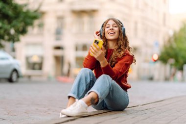 Genç, neşeli, güzel bir kadın dans ediyor ve kulaklıkla en sevdiği müziği dinliyor. Seyahat, turizm, teknoloji, blog konsepti. Kasaba yaşam tarzları.