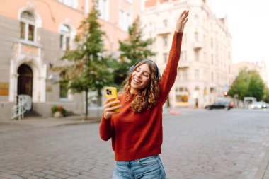 Genç, neşeli, güzel bir kadın dans ediyor ve kulaklıkla en sevdiği müziği dinliyor. Seyahat, turizm, teknoloji, blog konsepti. Kasaba yaşam tarzları.