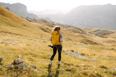 Kadın turist, sırt çantasıyla dağlarda durmuş manzarayı seyrediyor. Seyahat, yaşam tarzı, başarı, macera.