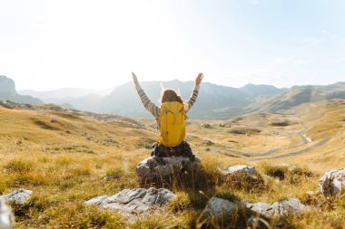Kadın turist, sırt çantasıyla dağlarda durmuş manzarayı seyrediyor. Seyahat, yaşam tarzı, başarı, macera.