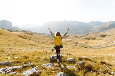 Kadın turist, sırt çantasıyla dağlarda durmuş manzarayı seyrediyor. Seyahat, yaşam tarzı, başarı, macera.