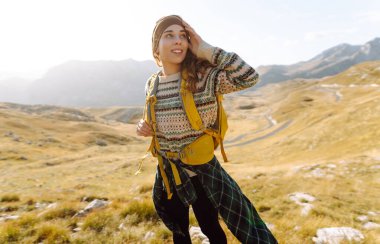 Kadın turist, sırt çantasıyla dağlarda durmuş manzarayı seyrediyor. Seyahat, yaşam tarzı, başarı, macera.