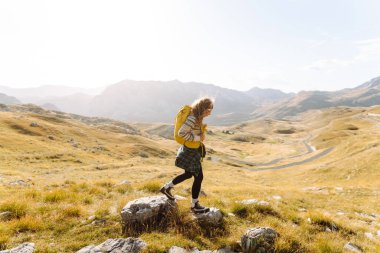 Kadın turist, sırt çantasıyla dağlarda durmuş manzarayı seyrediyor. Seyahat, yaşam tarzı, başarı, macera.
