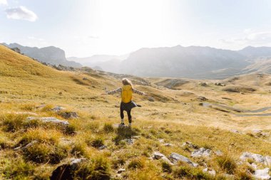 Kadın turist, sırt çantasıyla dağlarda durmuş manzarayı seyrediyor. Seyahat, yaşam tarzı, başarı, macera.
