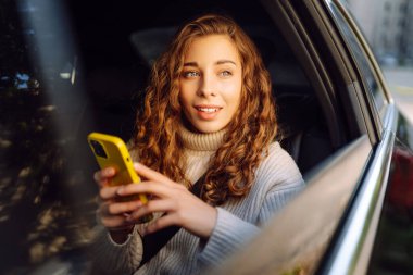 Güzel bir kadının arka koltuklarda akıllı telefon kullanarak oturduğu rahatlatıcı bir an. Teknoloji kavramı, araba ve iş seyahati..