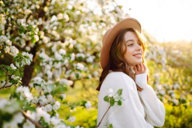Çiçek açan bahar bahçesinde kokunun tadını çıkaran mutlu kadın. Gençlik, aşk, moda, romantik ve yaşam tarzı konsepti