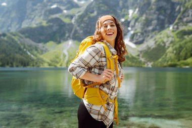 Güzel bir göl kenarında duran sırt çantalı güzel bir beyaz kadın yürüyüşçü. Aktif hayat. Seyahat, turizm, yürüyüş.
