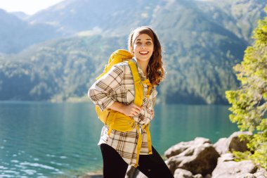 Güzel bir göl kenarında duran sırt çantalı güzel bir beyaz kadın yürüyüşçü. Aktif hayat. Seyahat, turizm, yürüyüş.