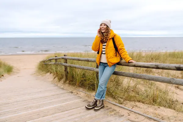 Soğuk havada deniz kenarında poz veren sarı ceketli bir kadın turist. Seyahat, yaşam tarzı, macera