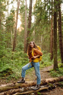 Ormanda ağaçların arasında yürürken sırt çantası taşıyan genç bir kadın. Yürüyüş, doğa, aktif yaşam tarzı