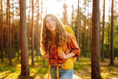 Ormanda ağaçların arasında yürürken sırt çantası taşıyan genç bir kadın. Yürüyüş, doğa, aktif yaşam tarzı