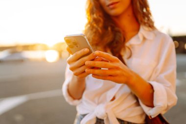 Genç bir kadın akıllı telefon tarayıcı uygulaması tutuyor ve sosyal medyanın güzel günbatımını seyrediyor. Bloglama, iletişim, teknoloji