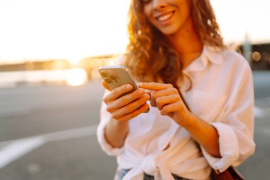 Genç bir kadın akıllı telefon tarayıcı uygulaması tutuyor ve sosyal medyanın güzel günbatımını seyrediyor. Bloglama, iletişim, teknoloji