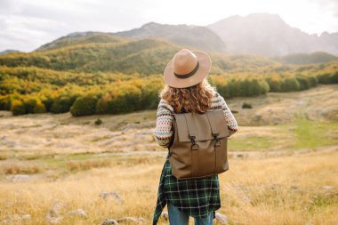 Kadın turistin sırt çantasıyla dağlarda durup manzarayı seyrettiği arka plan görüntüsü. Avrupa seyahati. Yaşam tarzı, tatil, turizm, doğa, aktif yaşam