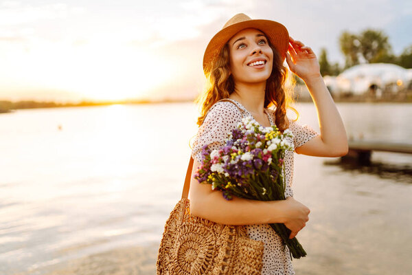 Счастливая молодая девушка в белом платье с букетом диких цветов гуляет по закату. Сельский стиль свадьбы
