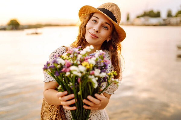 Счастливая молодая девушка в белом платье с букетом диких цветов гуляет по закату. Сельский стиль свадьбы