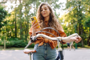 Mutlu kadın bisikletiyle gidip geliyor ve sokaklarda mutlu mesut telefon kullanıyor. Seyahat, hafta sonu, rahatlama ve yaşam tarzı konsepti. İşe giden yol.