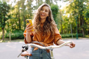 Mutlu kadın bisikletiyle gidip geliyor ve sokaklarda mutlu mesut telefon kullanıyor. Seyahat, hafta sonu, rahatlama ve yaşam tarzı konsepti. İşe giden yol.