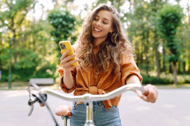 Mutlu kadın bisikletiyle gidip geliyor ve sokaklarda mutlu mesut telefon kullanıyor. Seyahat, hafta sonu, rahatlama ve yaşam tarzı konsepti. İşe giden yol.
