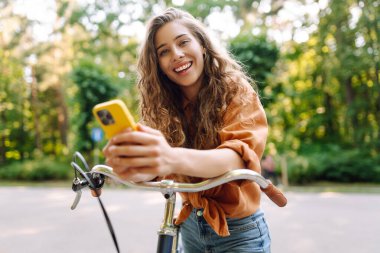 Mutlu kadın bisikletiyle gidip geliyor ve sokaklarda mutlu mesut telefon kullanıyor. Seyahat, hafta sonu, rahatlama ve yaşam tarzı konsepti. İşe giden yol.