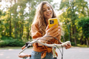Mutlu kadın bisikletiyle gidip geliyor ve sokaklarda mutlu mesut telefon kullanıyor. Seyahat, hafta sonu, rahatlama ve yaşam tarzı konsepti. İşe giden yol.