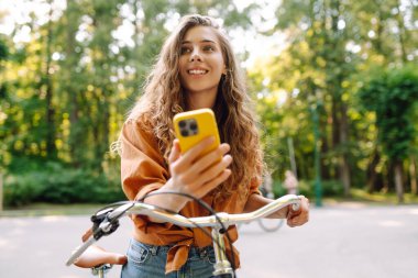 Mutlu kadın bisikletiyle gidip geliyor ve sokaklarda mutlu mesut telefon kullanıyor. Seyahat, hafta sonu, rahatlama ve yaşam tarzı konsepti. İşe giden yol.