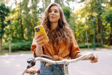 Mutlu kadın bisikletiyle gidip geliyor ve sokaklarda mutlu mesut telefon kullanıyor. Seyahat, hafta sonu, rahatlama ve yaşam tarzı konsepti. İşe giden yol.