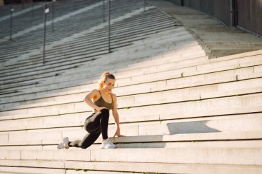 Açık havada egzersiz yapan zinde bir kadın. Parlak güneşli bir günde sporcu kıyafeti içinde mutlu bir şekilde gülümseyen bir sporcu işlevsel antrenman yapar. Spor, aktif yaşam, spor eğitimi, sağlıklı yaşam tarzı.