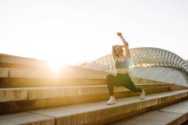 Açık havada egzersiz yapan zinde bir kadın. Parlak güneşli bir günde sporcu kıyafeti içinde mutlu bir şekilde gülümseyen bir sporcu işlevsel antrenman yapar. Spor, aktif yaşam, spor eğitimi, sağlıklı yaşam tarzı.