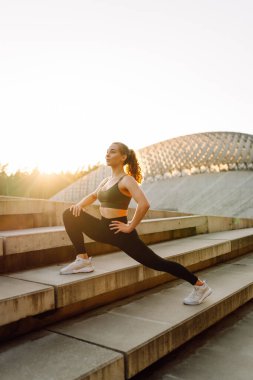 Açık havada egzersiz yapan zinde bir kadın. Parlak güneşli bir günde sporcu kıyafeti içinde mutlu bir şekilde gülümseyen bir sporcu işlevsel antrenman yapar. Spor, aktif yaşam, spor eğitimi, sağlıklı yaşam tarzı.