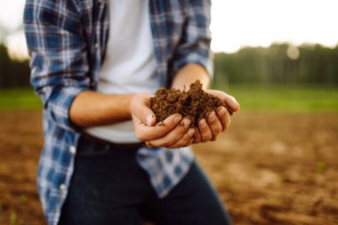 Bir tarlada verimli toprakları tutan bir çiftçinin ellerine yakın çekim. Bir tarım uzmanı ekmeden önce toprağın kalitesini kontrol eder. Tarım kavramı, kontrol ve analiz.