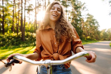 Neşeli bir kadın bisiklet sürüyor ve güneşli parkta selfie çekiyor. Güzel bir kadın dışarıda telefonla vakit geçiriyor. Selfie, boş zaman konsepti. Etkin yaşam biçimi.