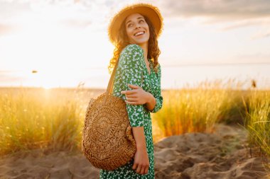 Parlak elbiseli ve şapkalı hoş bir kadın sahilde günbatımını seyrediyor. Mutlu kadın rahatlıyor ve dışarıda yürüyor. Dinlenme kavramı, özgürlük. Yaşam biçimi.