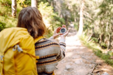 Sırt çantası ve elinde pusulayla dağ manzarası olan genç bir kadın yürüyüşçünün arka görüntüsü. Kadın yön bulmak için pusula kullanarak bir patika boyunca yürüyor. Etkin yaşam biçimi.