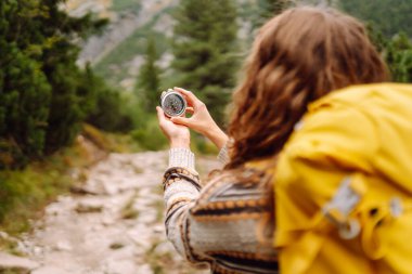Sırt çantası ve elinde pusulayla dağ manzarası olan genç bir kadın yürüyüşçünün arka görüntüsü. Kadın yön bulmak için pusula kullanarak bir patika boyunca yürüyor. Etkin yaşam biçimi.