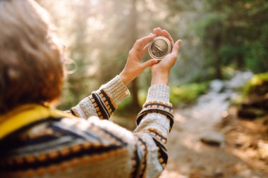 Sırt çantası ve elinde pusulayla dağ manzarası olan genç bir kadın yürüyüşçünün arka görüntüsü. Kadın yön bulmak için pusula kullanarak bir patika boyunca yürüyor. Etkin yaşam biçimi.