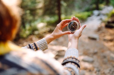 Sırt çantası ve elinde pusulayla dağ manzarası olan genç bir kadın yürüyüşçünün arka görüntüsü. Kadın yön bulmak için pusula kullanarak bir patika boyunca yürüyor. Etkin yaşam biçimi.