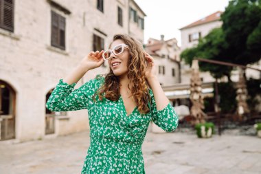 Yeşil elbiseli ve geniş kenarlı şapkalı neşeli bir kadın şehir meydanında dönüyor. Genç bir turist Avrupa caddelerinde yürümekten zevk alıyor. Seyahat, tatil konsepti.