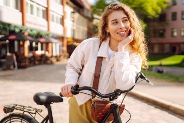 Güneşli bir günde genç bir turist Avrupa sokaklarında bisiklet sürüyor. Şık kıyafetler içindeki güzel bir kadın dışarıda eğleniyor. Yürüme konsepti. Etkin yaşam biçimi.