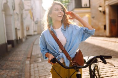 Güneşli bir günde genç bir turist Avrupa sokaklarında bisiklet sürüyor. Şık kıyafetler içindeki güzel bir kadın dışarıda eğleniyor. Yürüme konsepti. Etkin yaşam biçimi.