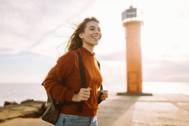Sırt çantalı hoş bir kadın deniz fenerinde günbatımının tadını çıkarıyor, özgürlüğü hissediyor. Turist doğada dinleniyor, sette yürüyor. Yürüme, seyahat, özgürlük kavramı. Yaşam biçimi.