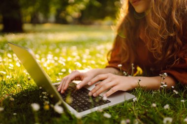 Yeşil çimenlikteki güneşli bir parkta dizüstü bilgisayarı olan mutlu bir kadın. Genç bayan serbest çalışan dışarıda havanın tadını çıkarıyor. Uzaktan çalışma konsepti. Etkin yaşam biçimi.