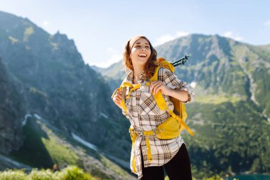 Genç bayan yürüyüşçü, renkli sırt çantasıyla dağda dikilen özgürlüğü hissediyor. Güneşli bir günde yemyeşil dağların nefes kesici manzarasından hoşlanan güzel bir kadın. Yürüyüş, özgürlük konsepti.