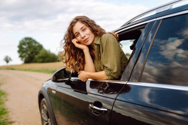 Arabasının camından sarkan özgürlüğünü hisseden güzel bir kadın. Genç bayan gezgin kırsal bölge ve araba macerasının tadını çıkarıyor. Yolculuk, özgürlük konsepti.