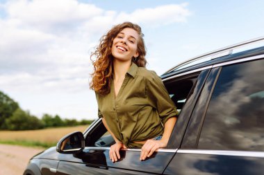 Arabasının camından sarkan özgürlüğünü hisseden güzel bir kadın. Genç bayan gezgin kırsal bölge ve araba macerasının tadını çıkarıyor. Yolculuk, özgürlük konsepti.