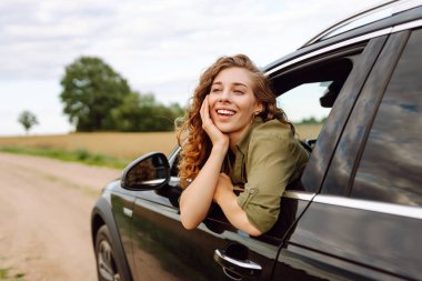 Arabasının camından sarkan özgürlüğünü hisseden güzel bir kadın. Genç bayan gezgin kırsal bölge ve araba macerasının tadını çıkarıyor. Yolculuk, özgürlük konsepti.