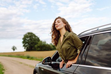 Arabasının camından sarkan özgürlüğünü hisseden güzel bir kadın. Genç bayan gezgin kırsal bölge ve araba macerasının tadını çıkarıyor. Yolculuk, özgürlük konsepti.