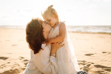 Neşeli anne ve kız gün batımı kumsalında birlikte eğleniyorlar. Küçük kızı olan güzel bir kadın dışarıda birlikte vakit geçiriyor. Çocukluk, eğlence, rahatlama konsepti.