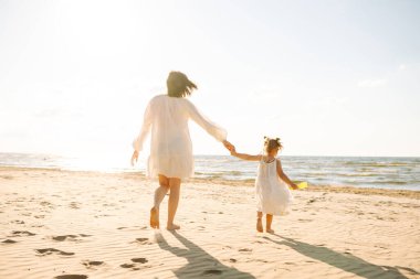 Neşeli anne ve kız gün batımı kumsalında birlikte eğleniyorlar. Küçük kızı olan güzel bir kadın dışarıda birlikte vakit geçiriyor. Çocukluk, eğlence, rahatlama konsepti.